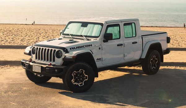 White Jeep Gladiator Rubicon parked on a sandy beach with ocean in the background