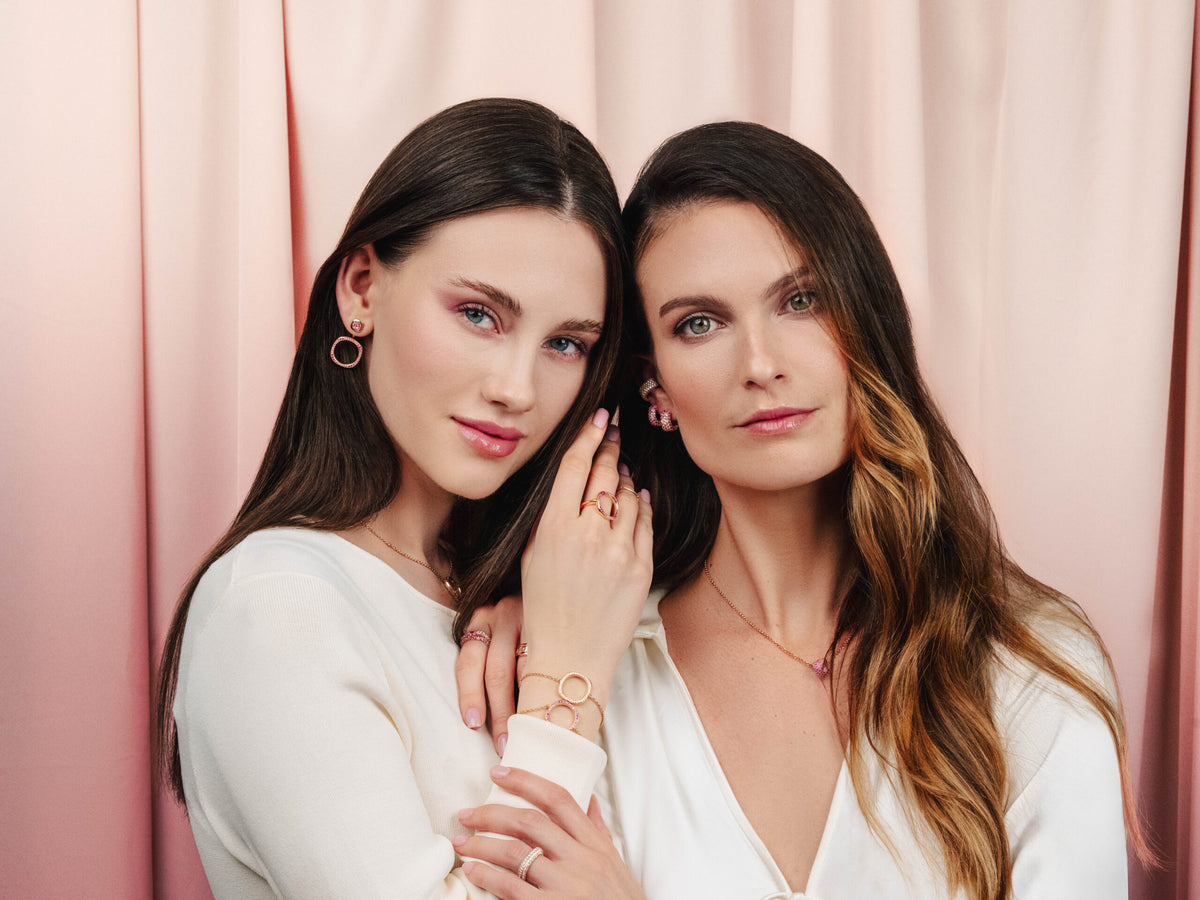 Two women posing closely against a pink curtain.